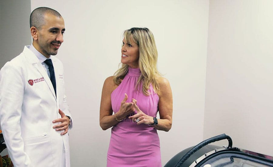 Dr. Babak Hajhosseini standing beside a hyperbaric oxygen therapy chamber at Wound and Burn Centers of America in Los Angeles.